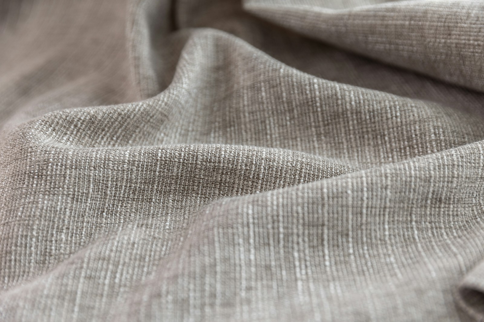 Stack of folded natural fibre garments including European linen shirts, undyed merino knitwear and a hemp denim jacket arranged on a pale wooden surface in soft north light.