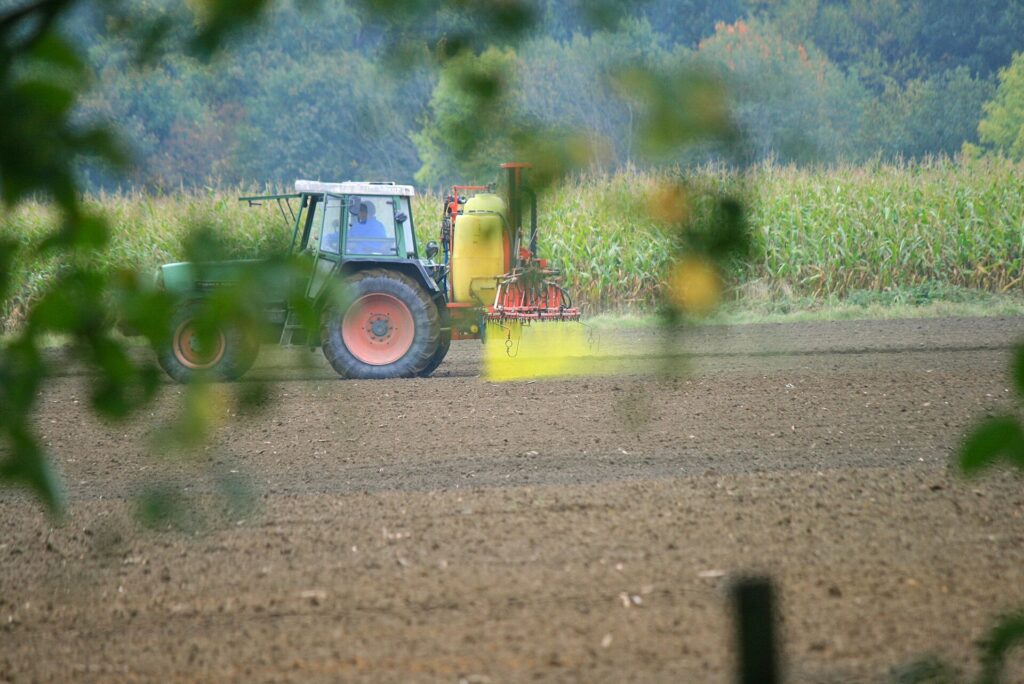 Trattore che percorre un campo coltivato con la barra di distribuzione aperta