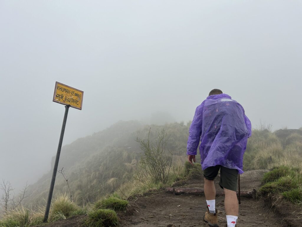 Escursionista con giacca tecnica sotto la pioggia su un sentiero di montagna