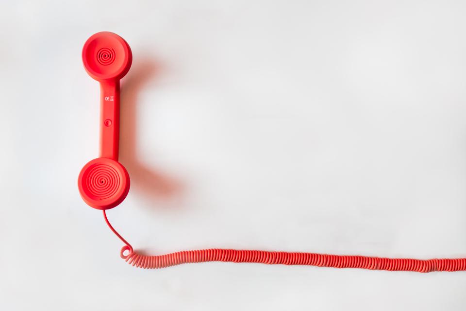 Cornetta di un telefono fisso appoggiata accanto a un foglio con un numero scritto