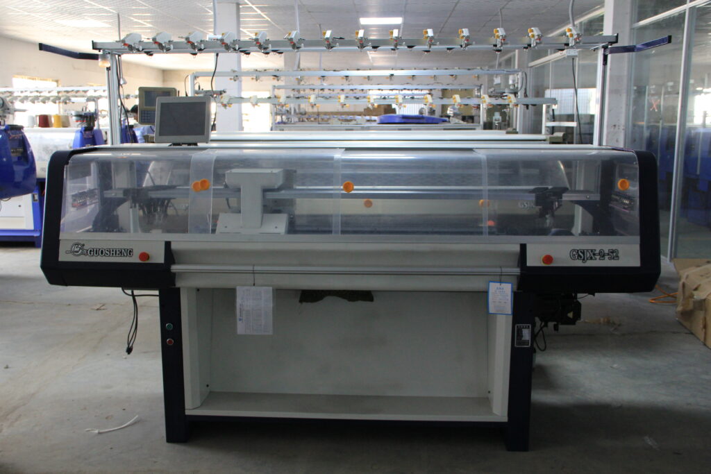 Macchina rettilinea per maglieria in funzione in un reparto di produzione tessile