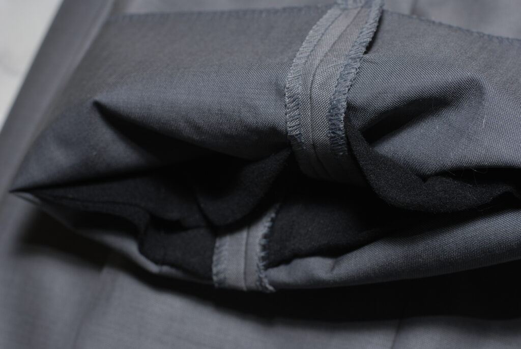 Pantaloni grigi in lana appesi a una gruccia di legno davanti a una parete chiara